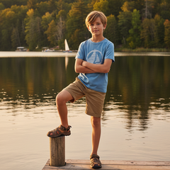 Young boy standing on a dock by a lake with trees in the background