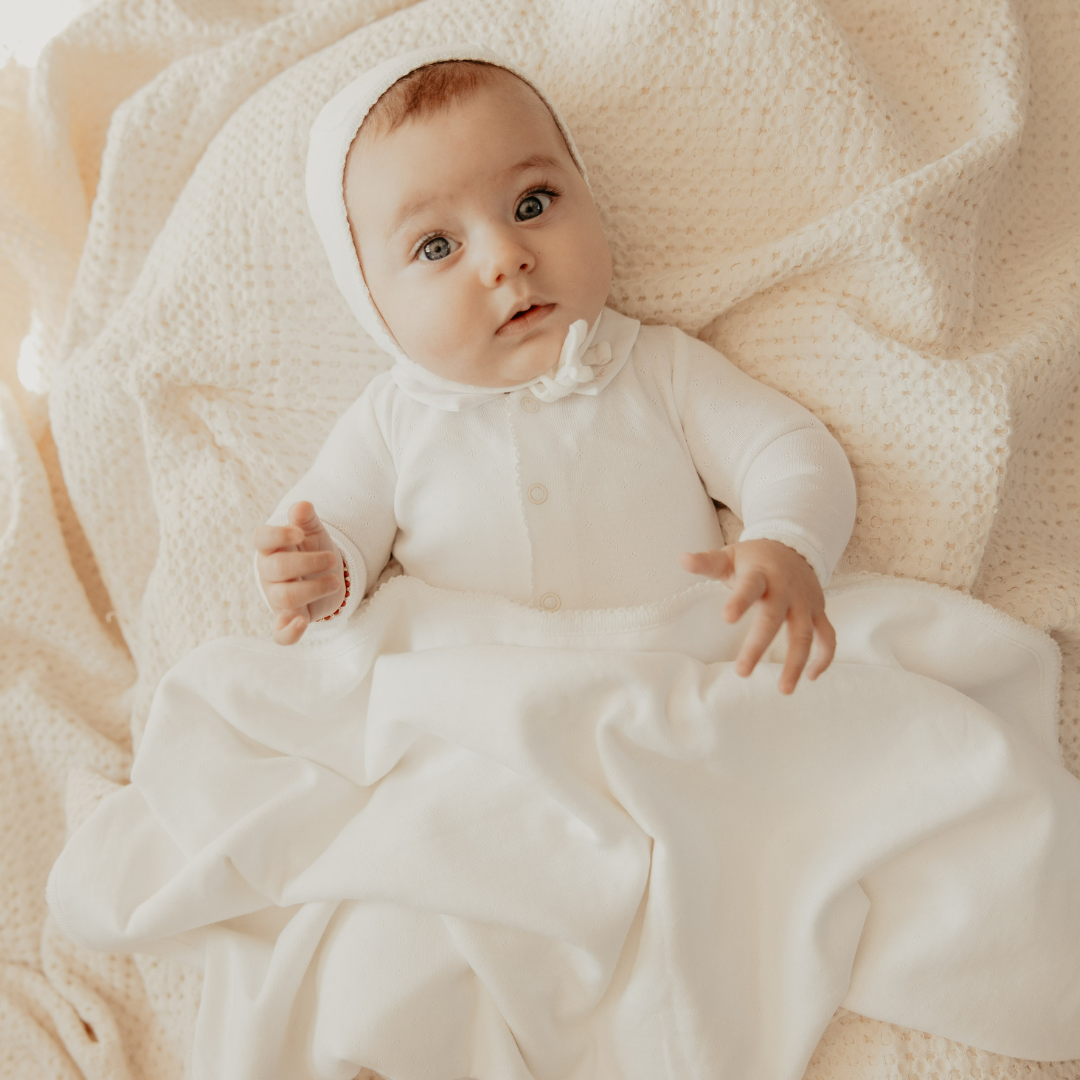 Baby in a white outfit lying on a soft beige blanket