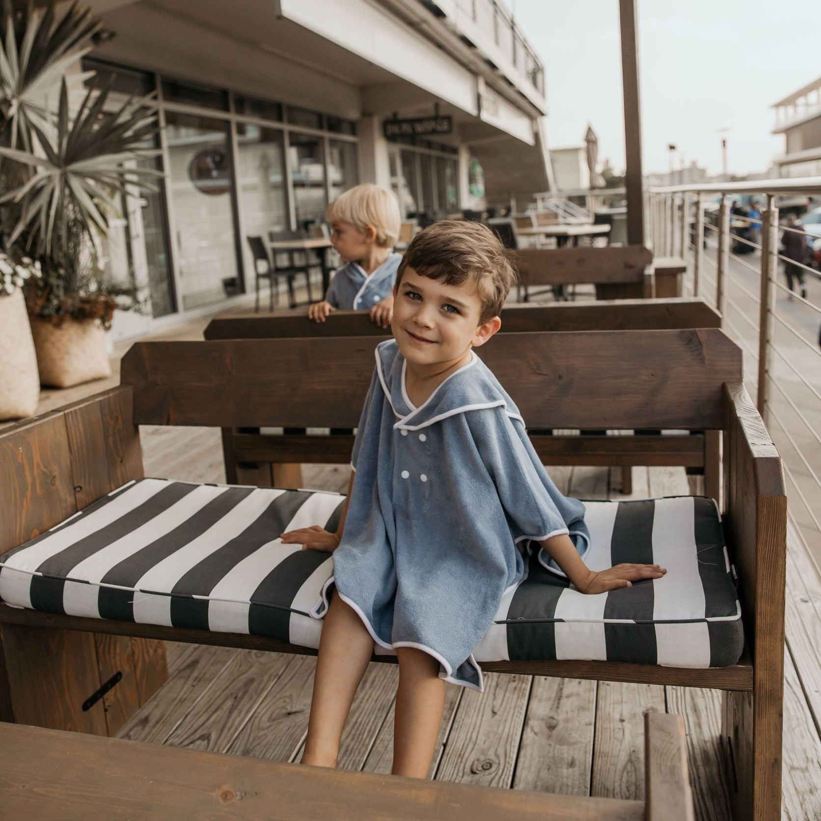 Child in a blue dress sitting on a striped bench outdoors.