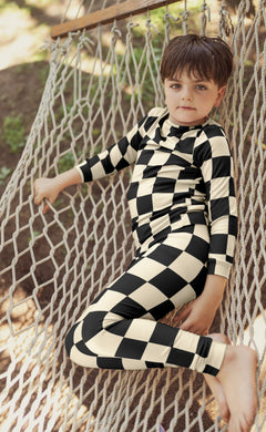 Child wearing a black and white checkered outfit sitting on a hammock.