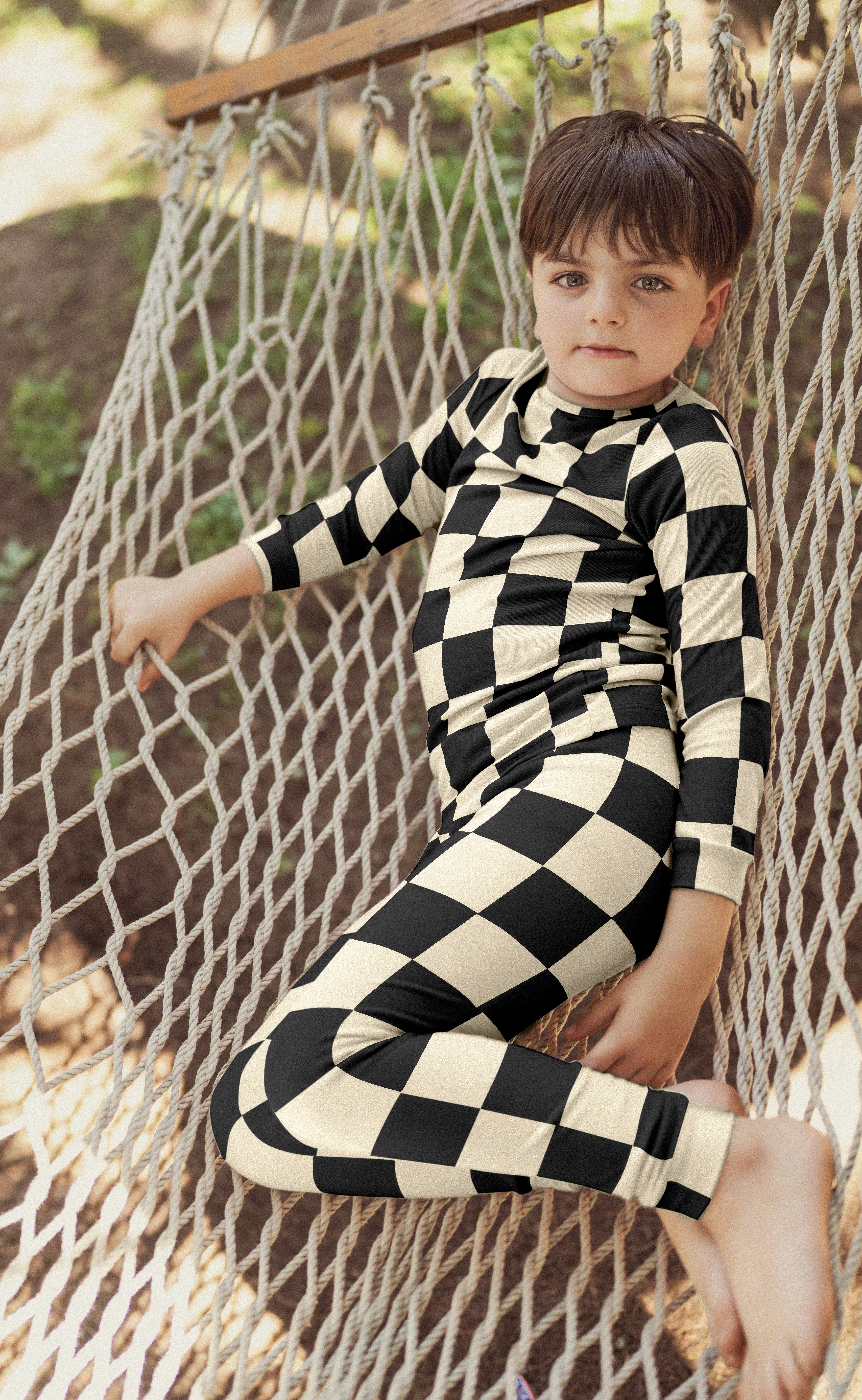 Child wearing a black and white checkered outfit sitting on a hammock.