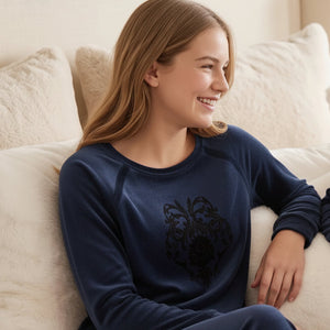 Two young girls in matching pink pajamas with a black design sitting on a couch.