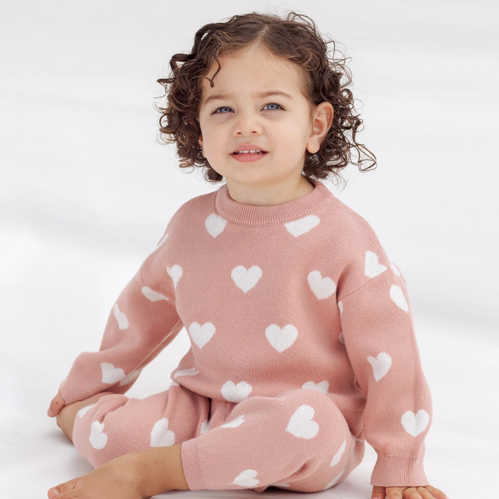 Child wearing a pink sweater with white heart patterns on a white background
