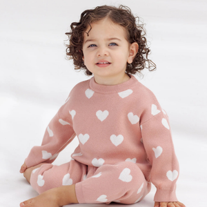 Child wearing a pink sweater with white heart patterns on a white background