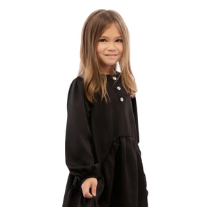 Young girl wearing a black dress with white buttons on a white background