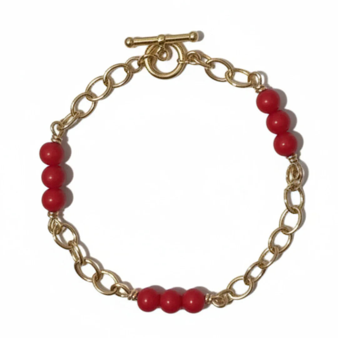 Gold chain bracelet with red beads on a white background