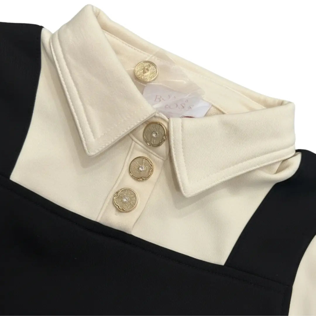 Close-up of a black and white garment with a cream collar and gold buttons, featuring a brand label.