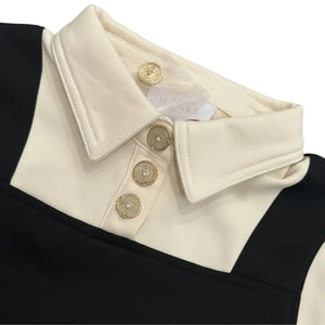 Close-up of a black and white garment with a cream collar and gold buttons, featuring a brand label.