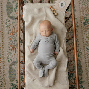 A newborn baby boy resting comfortably wearing the Aurora blue footie and beanie set.