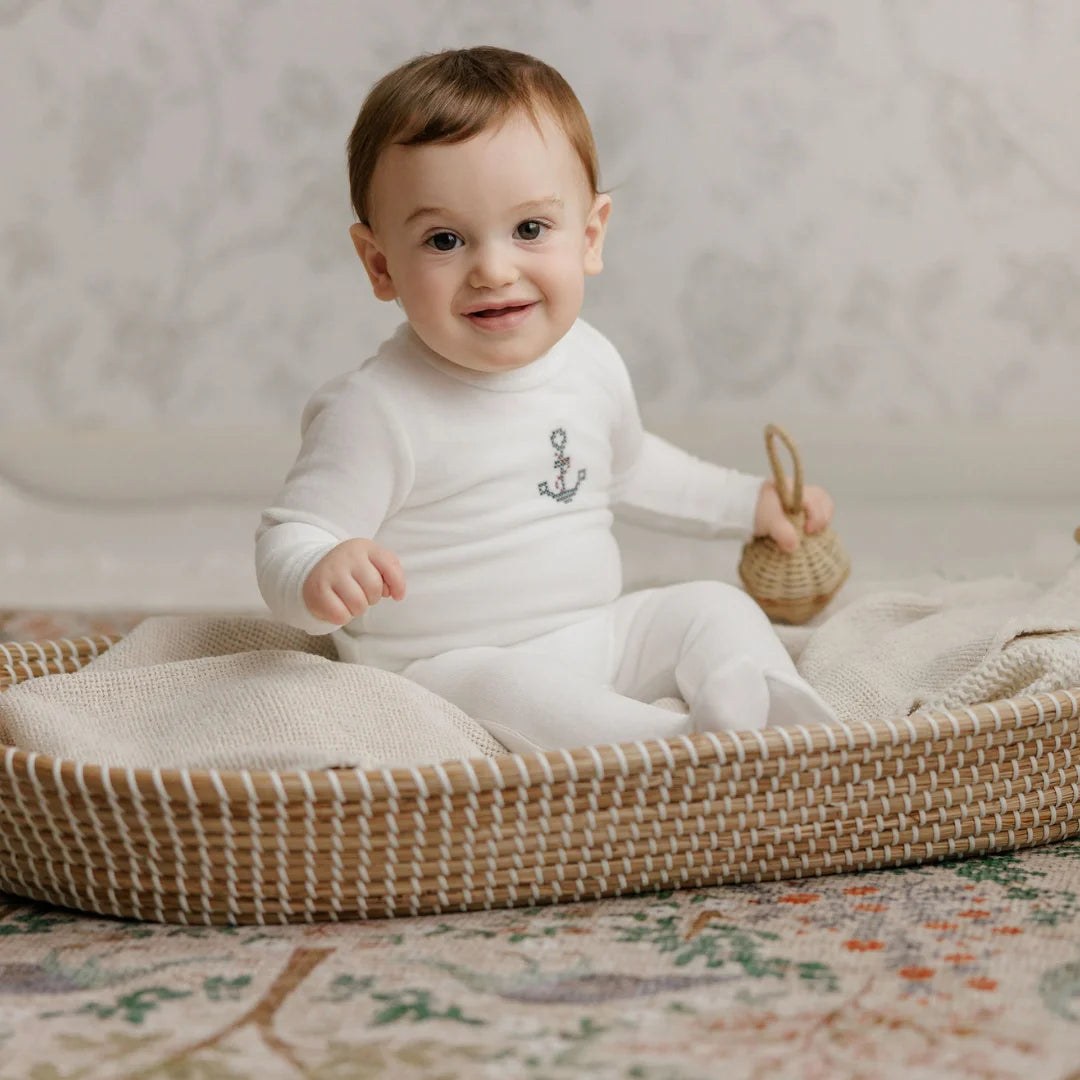 A newborn baby boy resting comfortably wearing the Aurora ivory footie and beanie set.