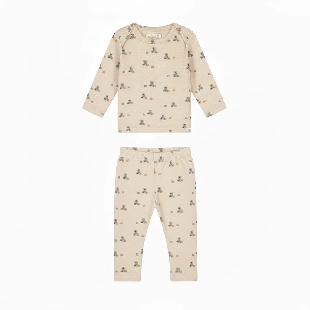 A long-sleeve baby t-shirt in cream-colored cotton with a small teddy bear and block print pattern, shown flat on a white background.