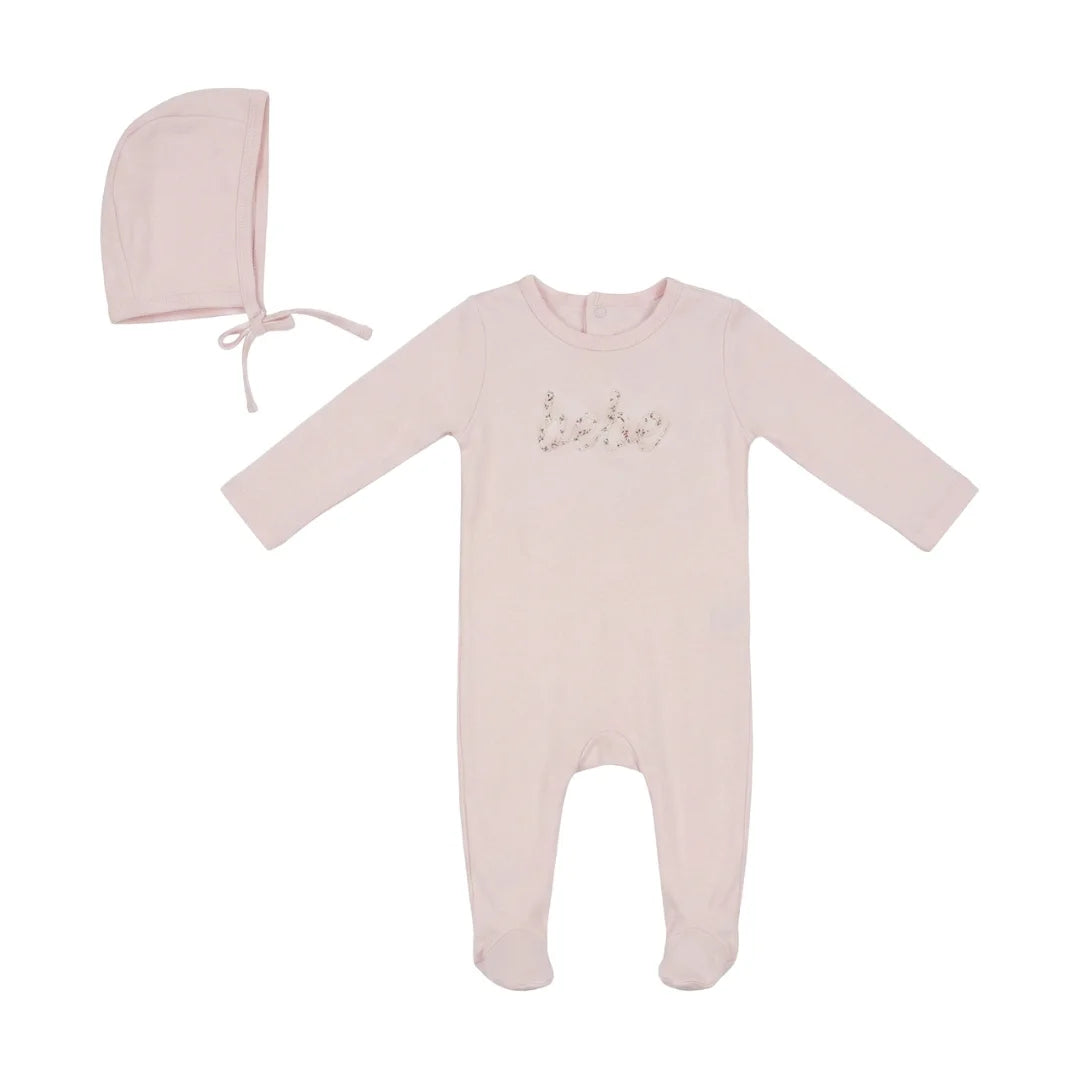 A baby footed sleeper in pale pink with 'baby' written across the chest in a glittery script, accompanied by a matching bonnet hat, displayed on a clean white background.