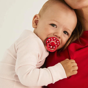 Baby with a red pacifier held by an adult against a white background