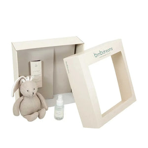A baby gift set featuring a beige plush bunny, a small clear bottle with a white dropper cap, and a cream-colored gift box with a windowed lid. The brand name 'bimbr dreams' is printed on the lid.
