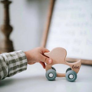 Hand holding a wooden toy car with 'Callio' branding on a light background