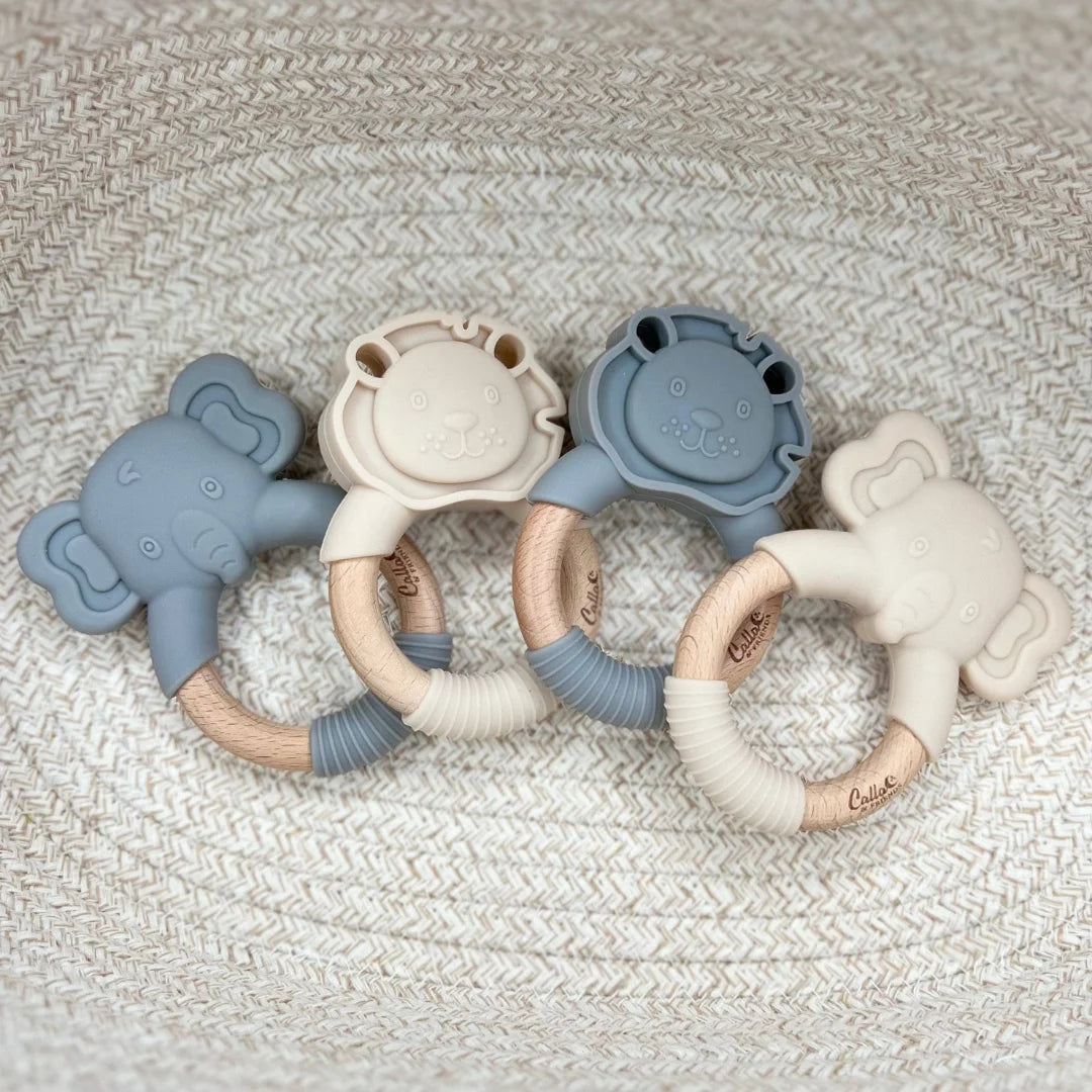 Four silicone baby teething rings in blue and beige on a textured surface