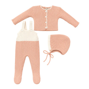 Baby outfit set with pink cardigan, white bib overalls, and matching bonnet on a white background