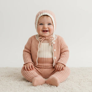 Baby wearing a pink knitted outfit with a matching bonnet on a white background
