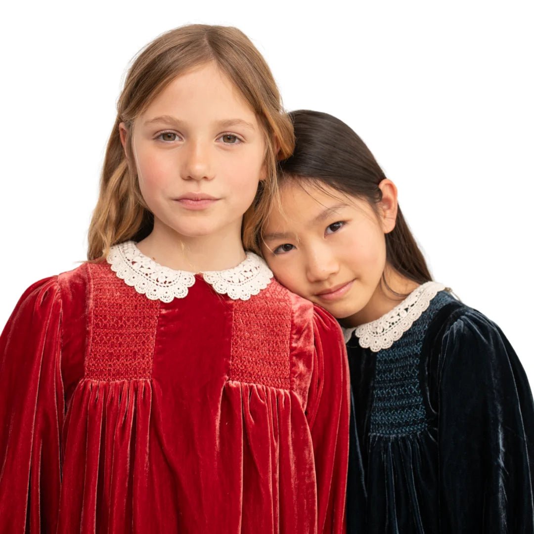 A little girl smiling while wearing the beautiful red Lory dress in a formal setting.