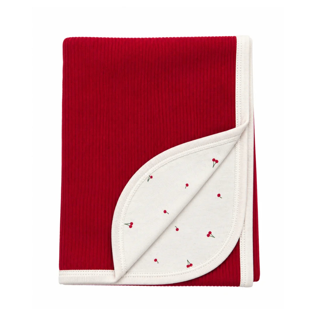 A flat-lay view of the Coton Pompom mini cherries corduroy blanket in coral.