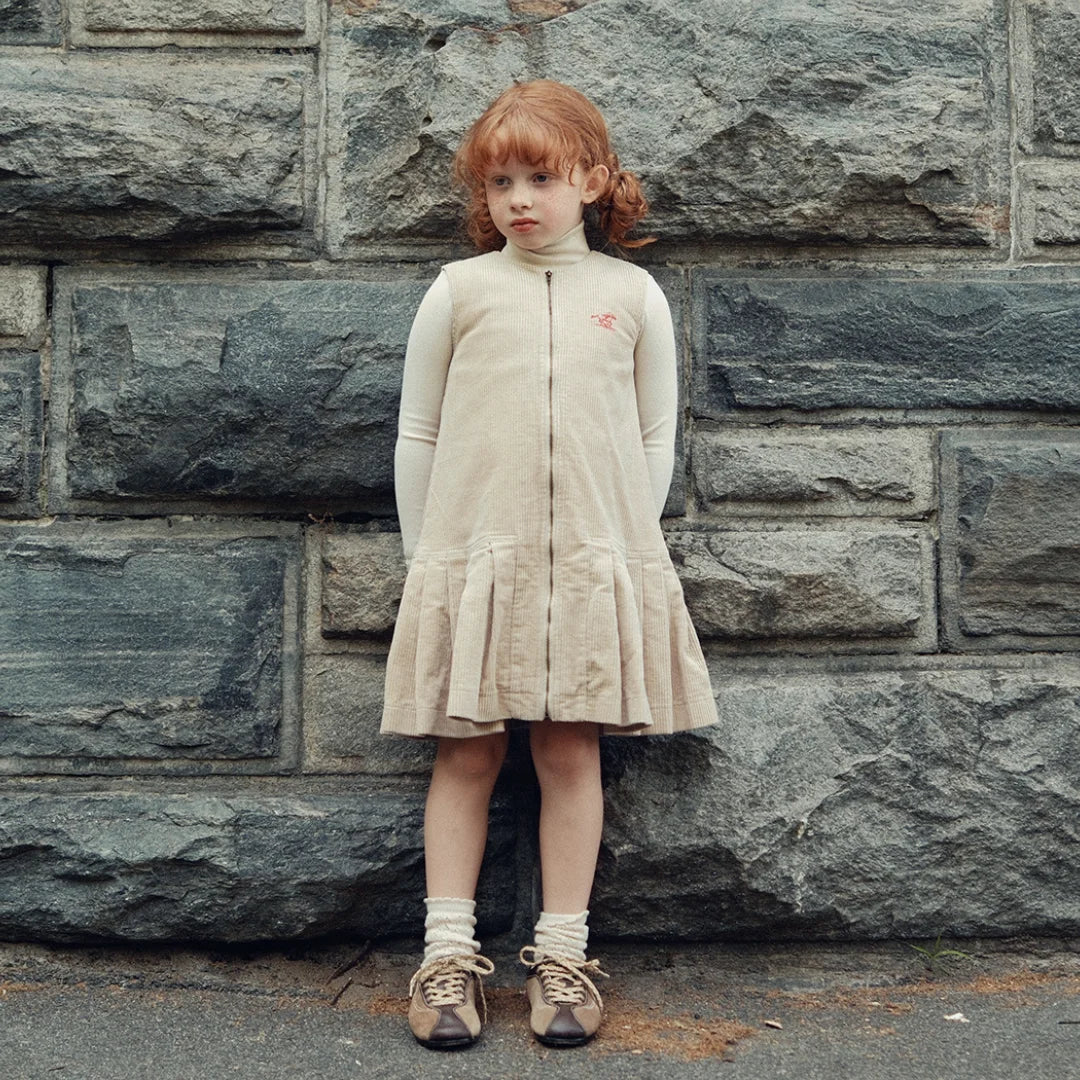 A child wearing the Cottier oatmilk dress modelling the dress a serene outdoor.