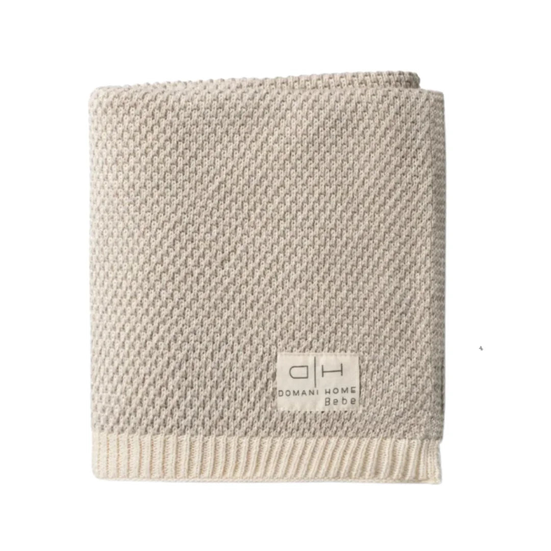 A folded beige textured knit blanket with a ribbed cream border and a small white brand label reading 'Domain Home Decor' on a plain white background.