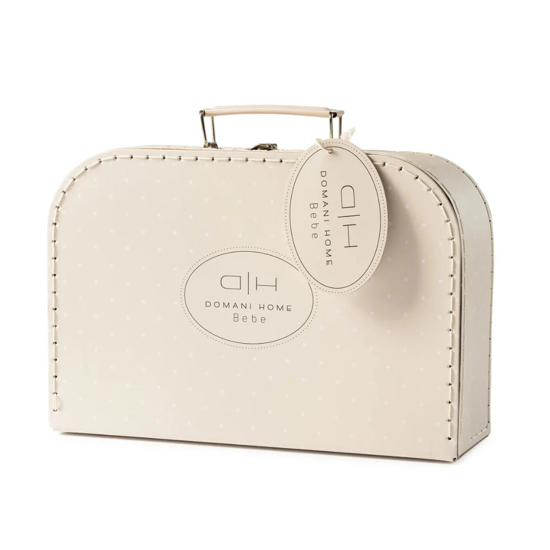 A cream-colored Domani Home Bebe suitcase-style bag with a top handle, decorative stitched edges, a small polka-dot pattern, and a hanging oval tag on a white background.