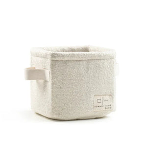 A square, open-top woven storage basket in a light oatmeal beige color, featuring a fabric handle on the left and a small brand label on the front right. The brand 'Domain Home Decor' is clearly visible on the label.