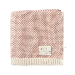 A folded woven blanket in a dusty pink and cream colorway, featuring a textured basketweave pattern and a cream ribbed border. A small white brand label reading 'DH DOMANI HOME BEDS' is stitched onto the front.