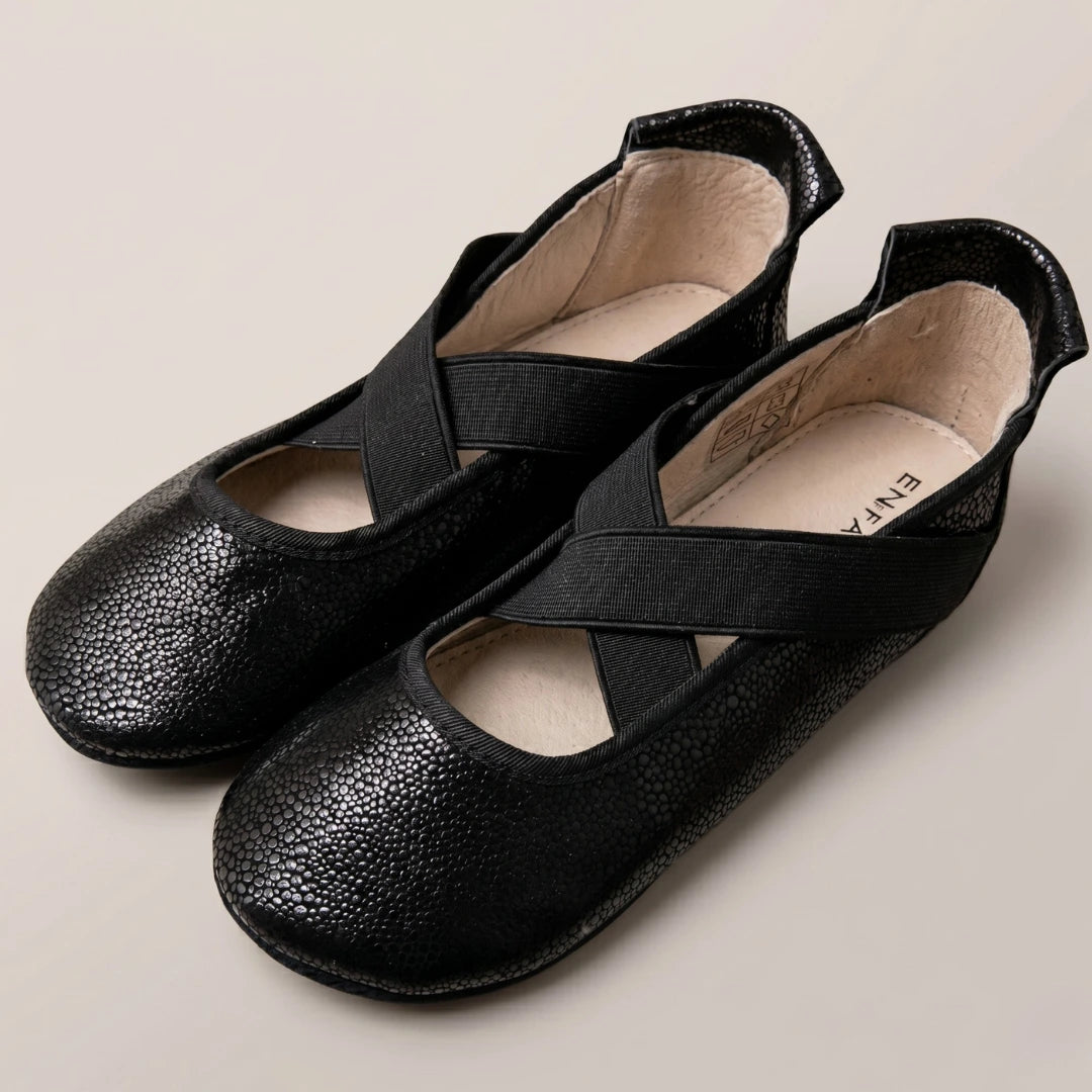 Pair of black shoes with cross straps on a beige background
