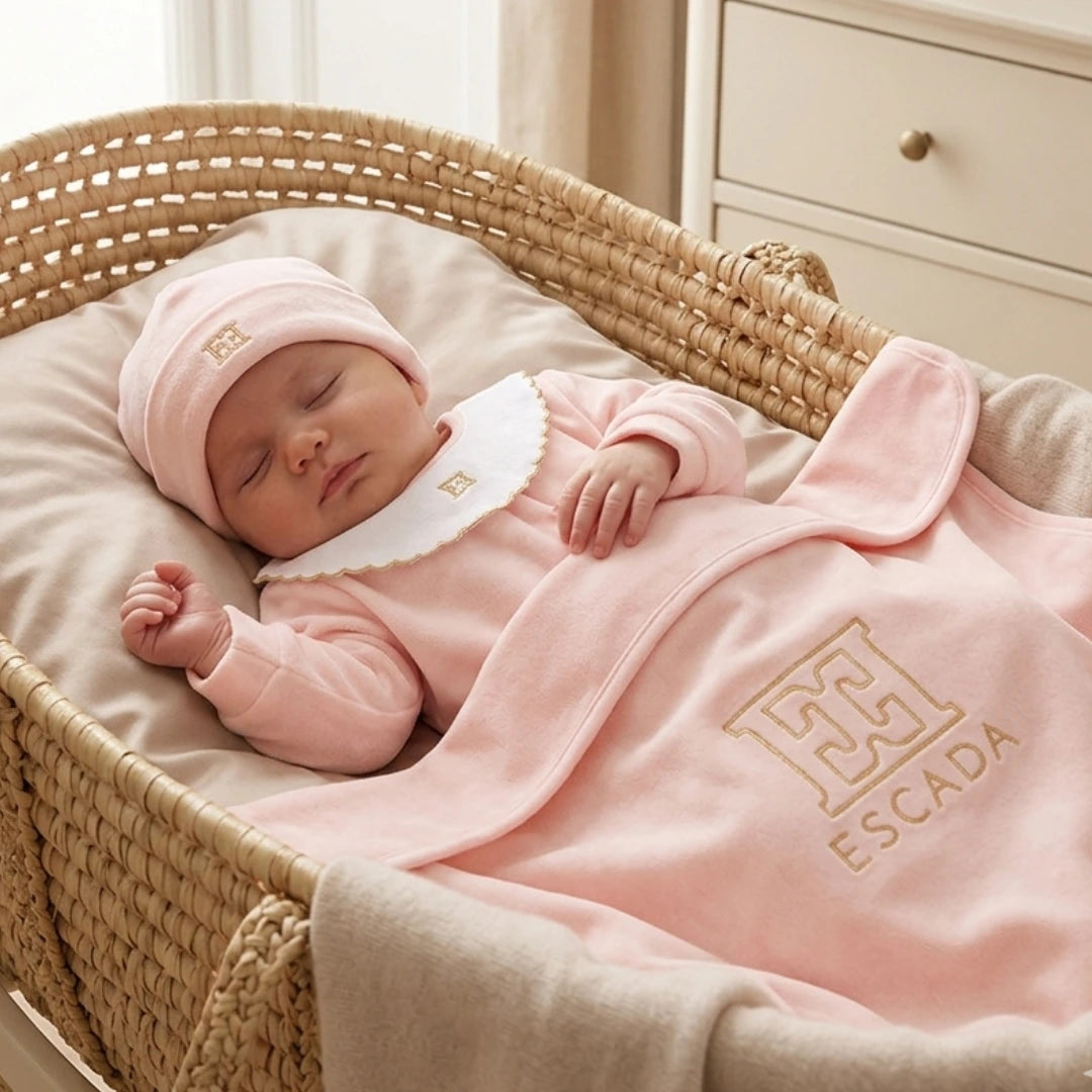 Baby in a pink outfit with Escada logo sleeping in a crib.