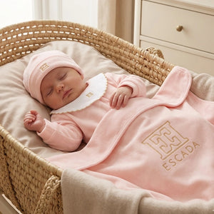 Baby in a pink outfit with Escada logo sleeping in a crib.