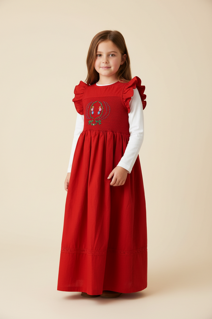 Young girl wearing a red dress with a white long-sleeve shirt underneath on a beige background