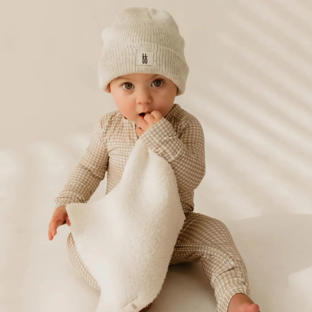 An infant holding the Forever French cream lovey in a modern nursery.