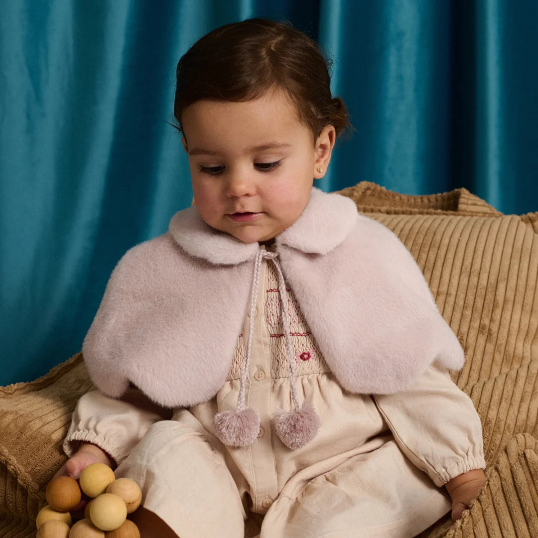 A young girl smiling in a festive setting while wearing the pink scalloped faux fur capelet.