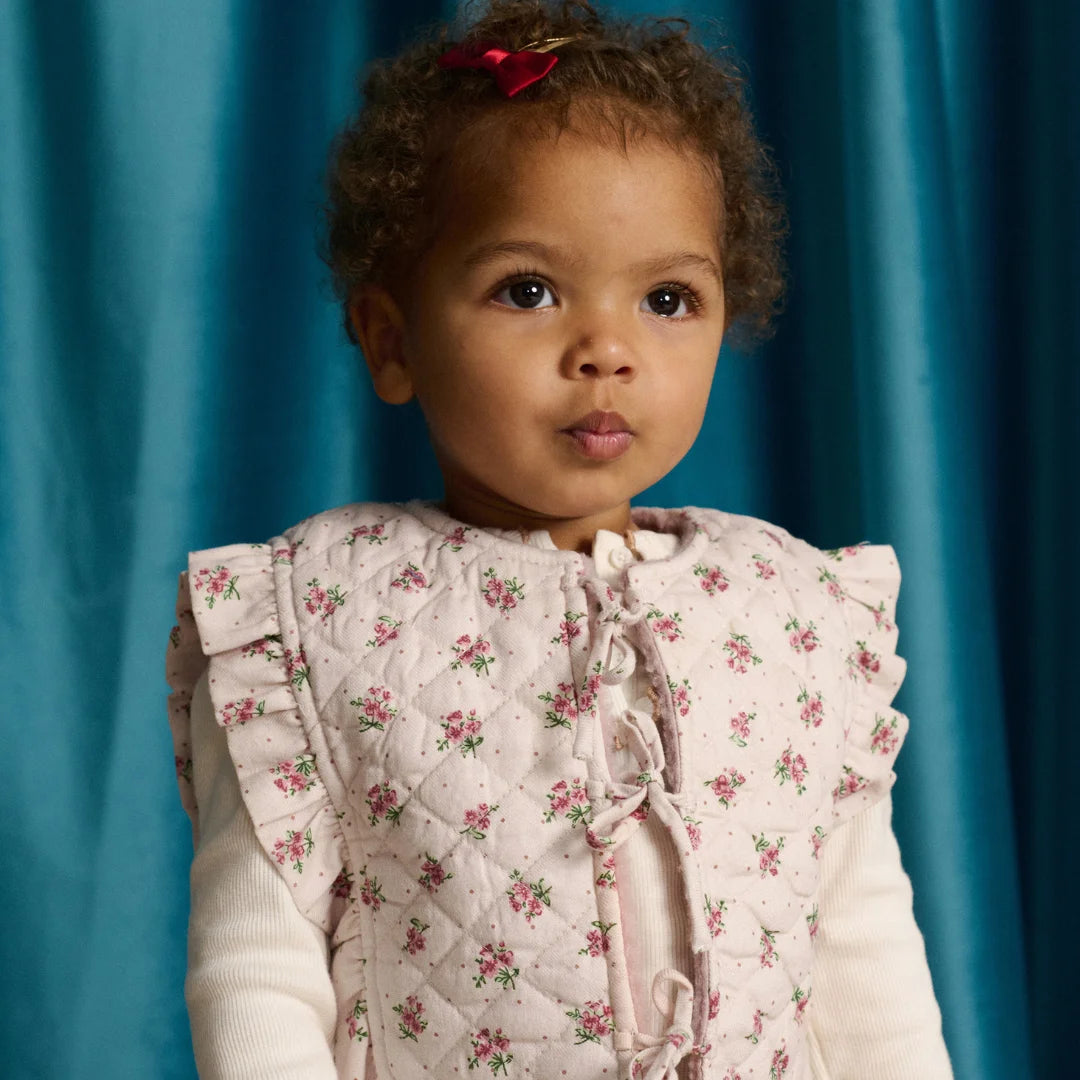 Young child wearing a floral quilted vest against a blue curtain background