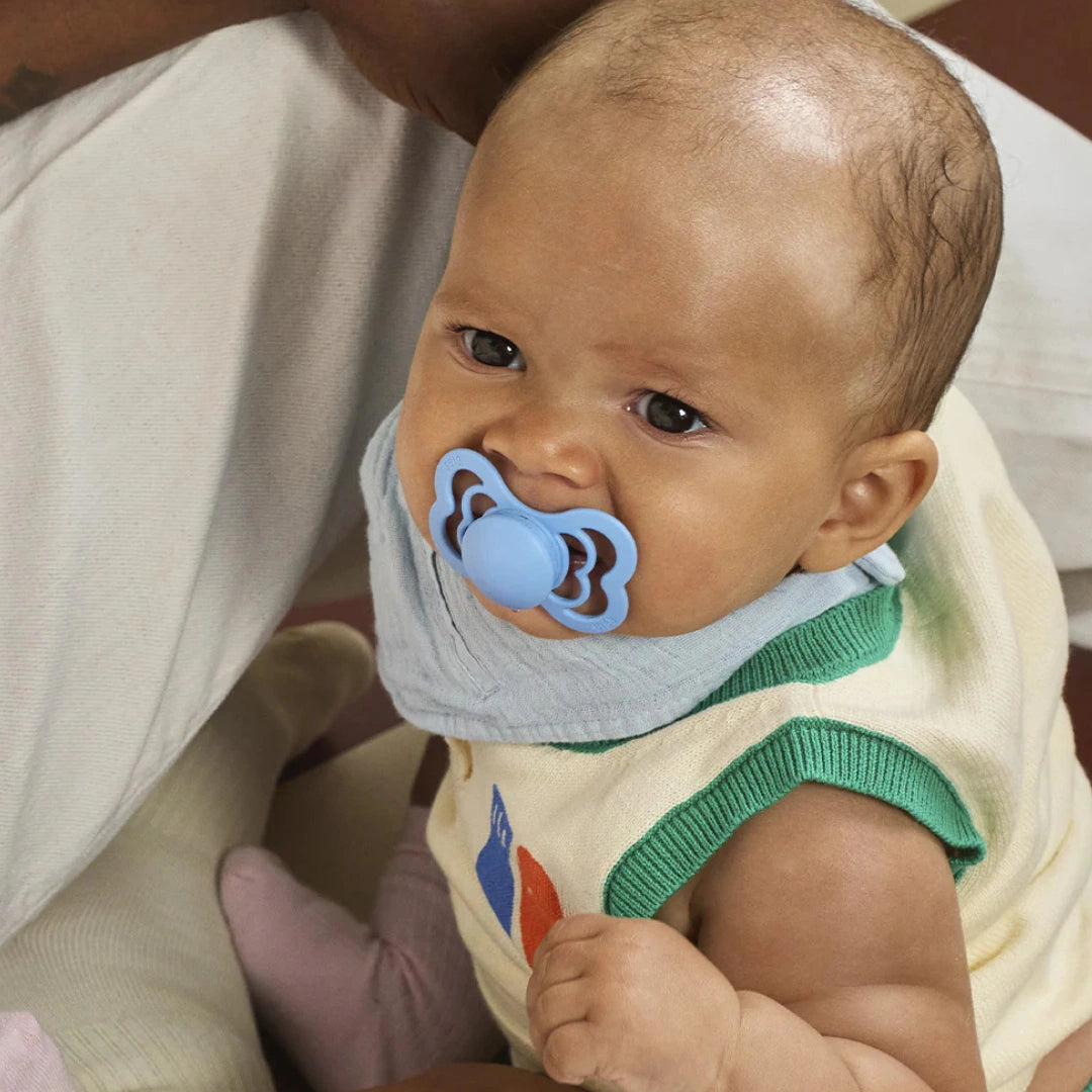 Baby wearing a blue pacifier with a person holding them