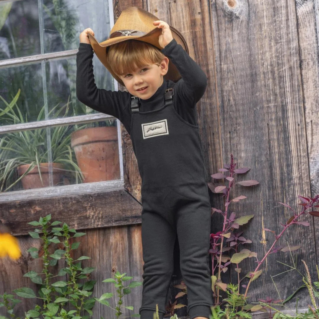 A child wearing the JayBee black sherpa patch overalls happily during an outdoor park outing.