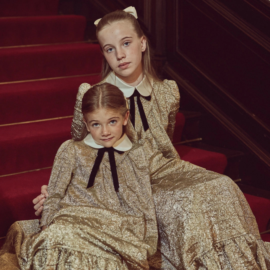 Two young girls in dark dresses standing in a room with decorative elements.