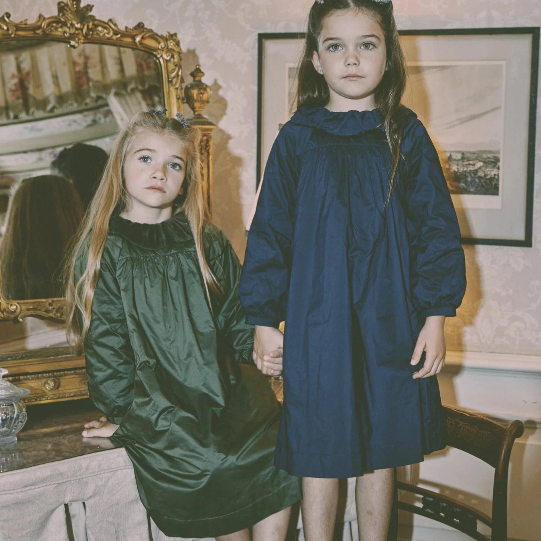 Two young girls in dark dresses standing in a room with decorative elements.