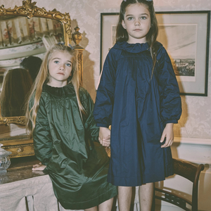 Two young girls in dark dresses standing in a room with decorative elements.