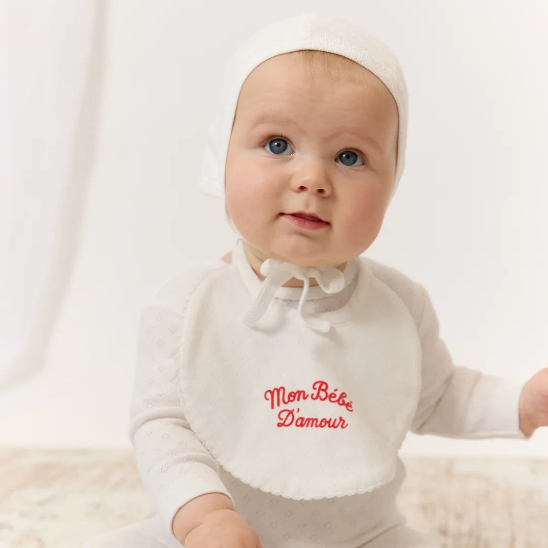 An infant wearing the Kipp red mon bebe bib comfortably during a mealtime feeding.