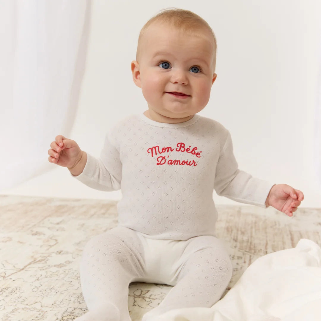 A newborn baby resting comfortably wearing the Kipp red baby footie and matching hat.