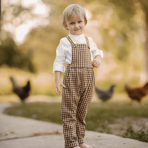 A child wearing the Lillies Dream gingham overalls happily during an outdoor outing.