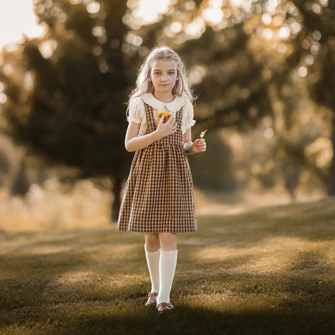 A child wearing the Lillies Dream gingham pinafore happily during an outdoor outing.