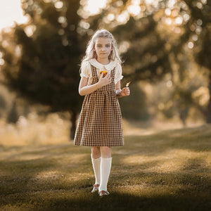 A child wearing the Lillies Dream gingham pinafore happily during an outdoor outing.