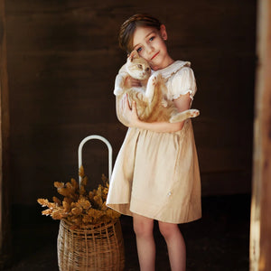 A child wearing the Lillies Dream parchment gingham pinafore happily during an outdoor outing.