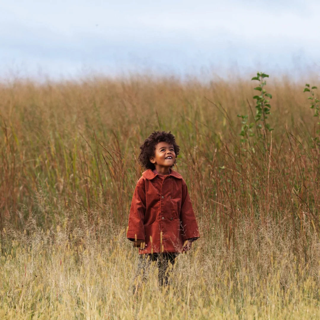 A child wearing the Lillies Dream rosewood corduroy coat happily during an outdoor outing.