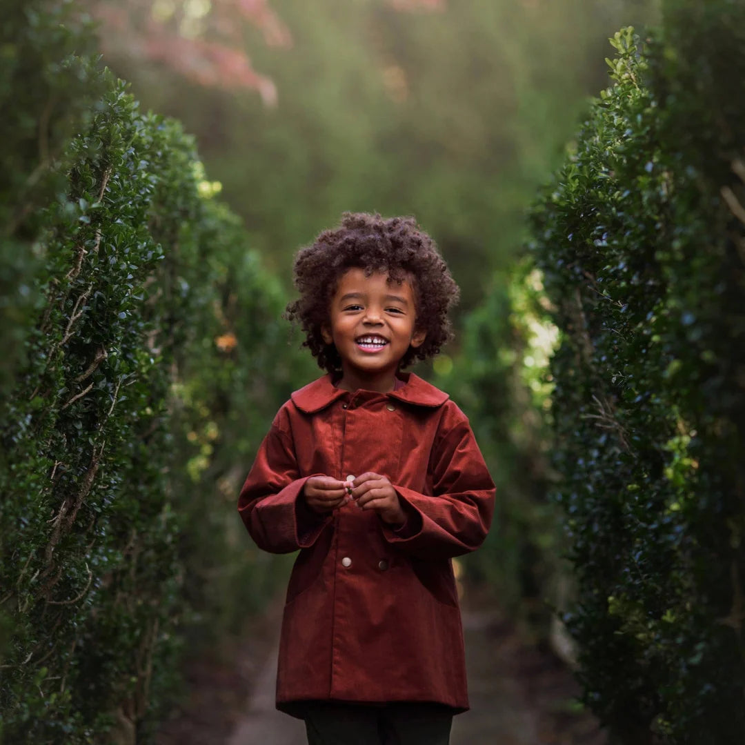 A child wearing the Lillies Dream rosewood corduroy coat happily during an outdoor outing.