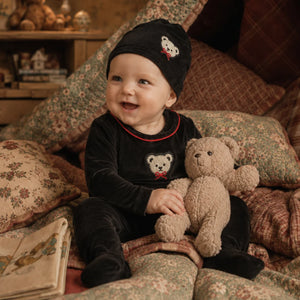 An infant resting peacefully while wearing the Little Label footie and hat set.